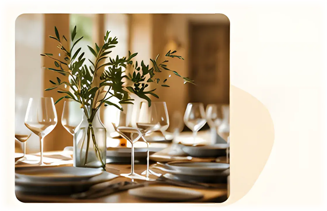 Restaurant table set with wine glasses and a vase of olive branches in a warm, wood-panelled dining room