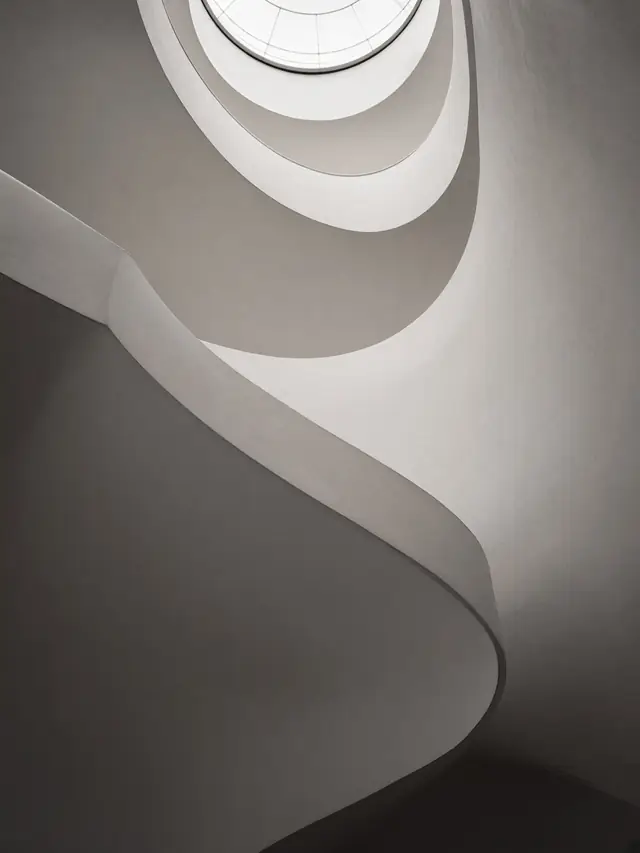 Looking up a white spiral staircase toward a round skylight