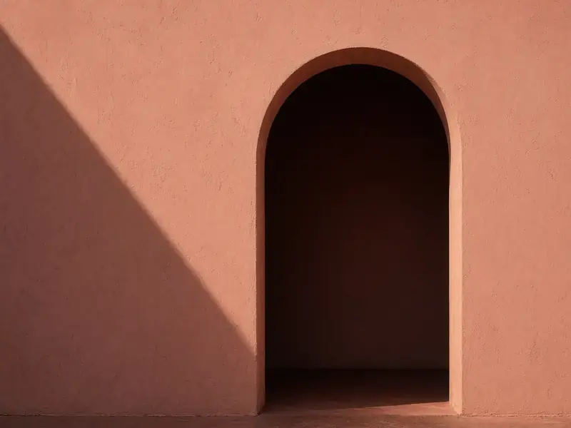 A terracotta plaster wall with an arched doorway and a sharp diagonal shadow