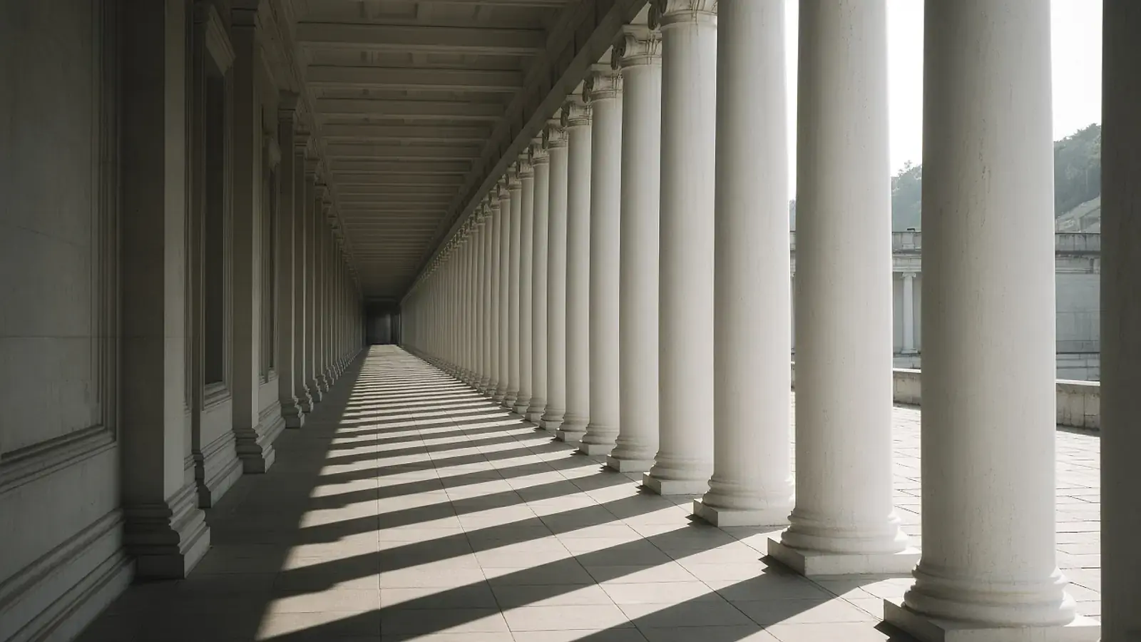 A long colonnade of white columns with stripes of sunlight on the stone floor