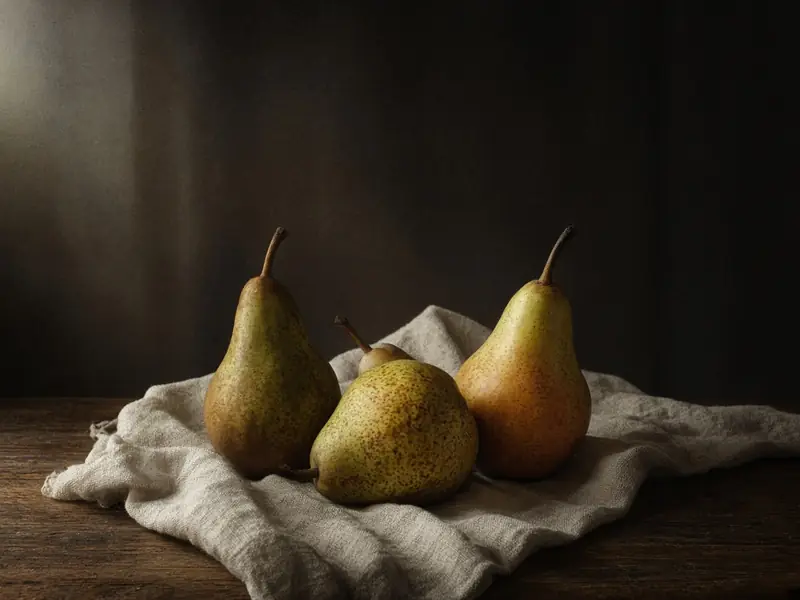 Pears on crumpled linen on a wooden table in soft window light